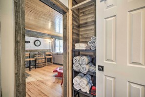 A room with wooden flooring, a red table, and a shelf with rolled towels. - Family Home - Walk to Town & Balsam Lake! (Balsam Lake)
