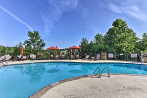 A swimming pool with lounge chairs and umbrellas, surrounded by trees and a fence. - Pigeon Forge Vacation Rental: 1 Mi to Dollywood (Pigeon Forge)