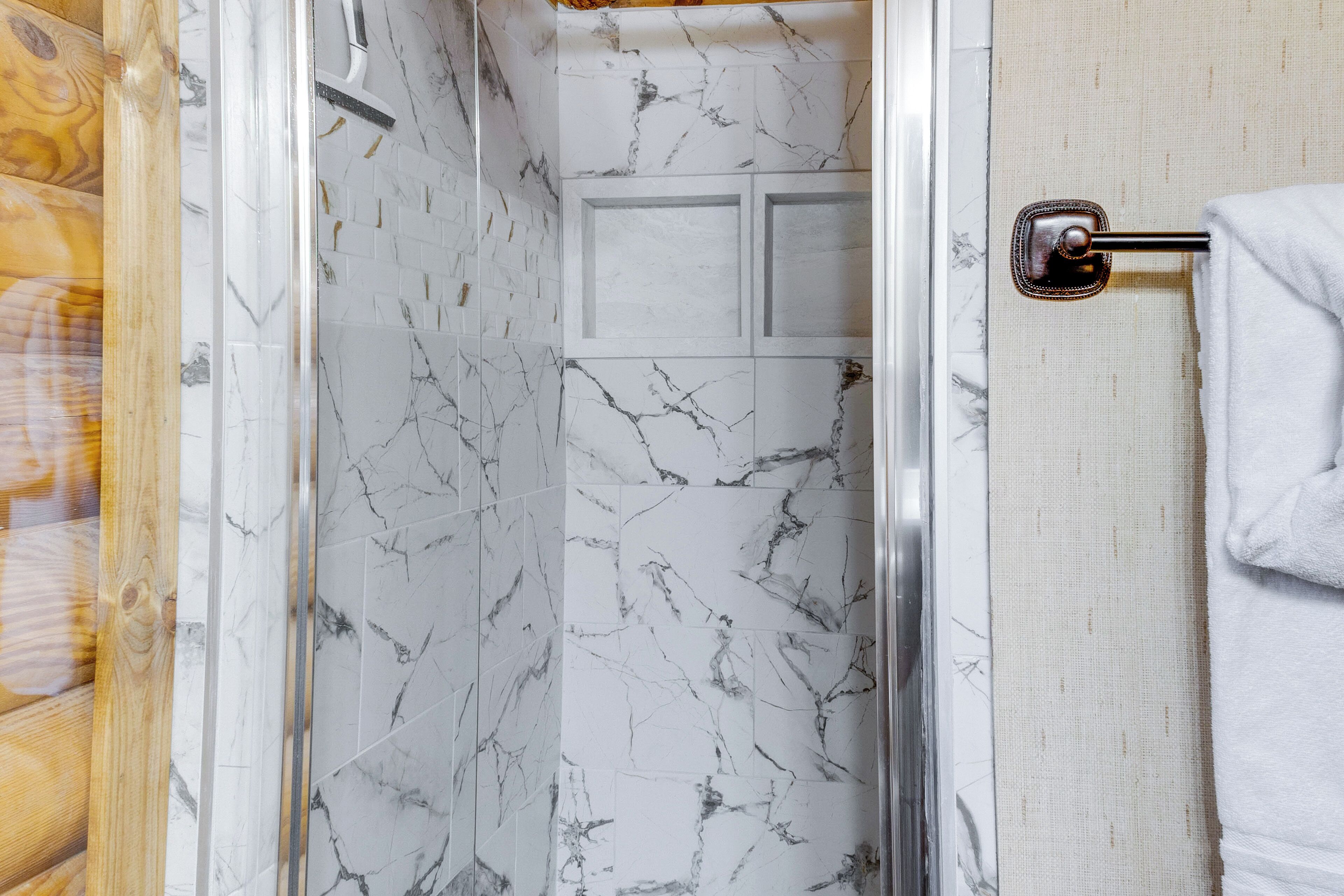 A bathroom with white marble tiles, a glass shower enclosure, and a towel rack.
