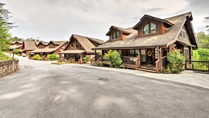 Une rangée de bâtiments de style chalet en rondins, dotés de toits pentus et de façades en bois, est disposée le long d’une route goudronnée, avec un mur de pierre d’un côté.