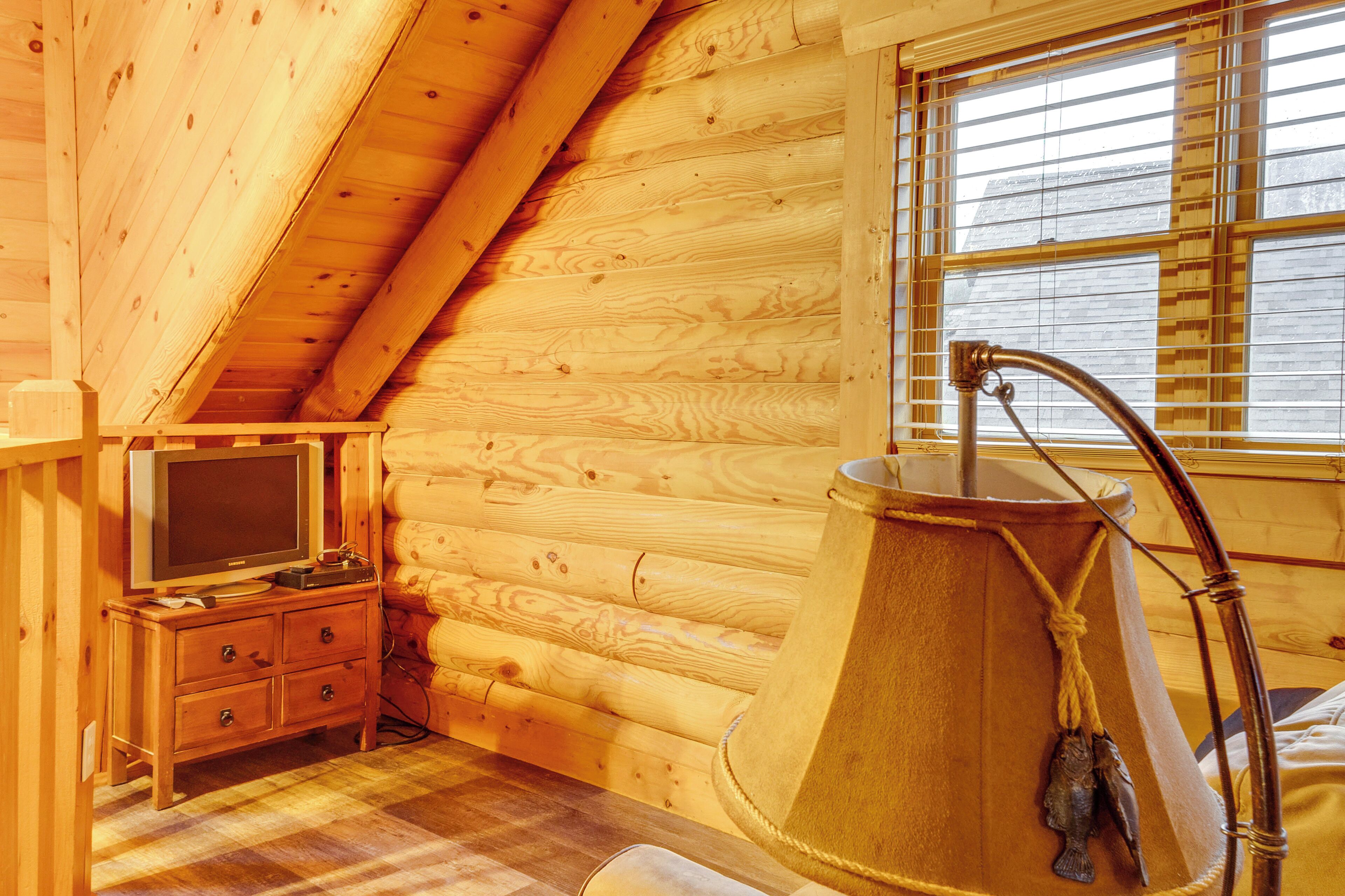 A cozy log cabin room with a wooden interior, a television on a dresser, and a large wooden tub.