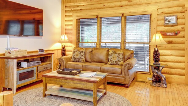L’intérieur d’un chalet confortable, avec des murs en rondins de bois, un canapé en bois, une table basse, un téléviseur et une statue d’ours.