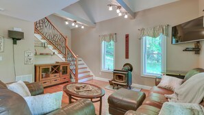 A spacious living room with a fireplace, leather sofas, a wooden staircase, and a television. - Game Room & Hot Tub: Old Forge Home! (Old Forge)