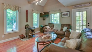 A cozy living room with a fireplace, leather sofas, and large windows offering a view of the outdoors. - Game Room & Hot Tub: Old Forge Home! (Old Forge)