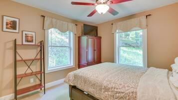 A bedroom with a bed, a ceiling fan, a wardrobe, and two windows with curtains.