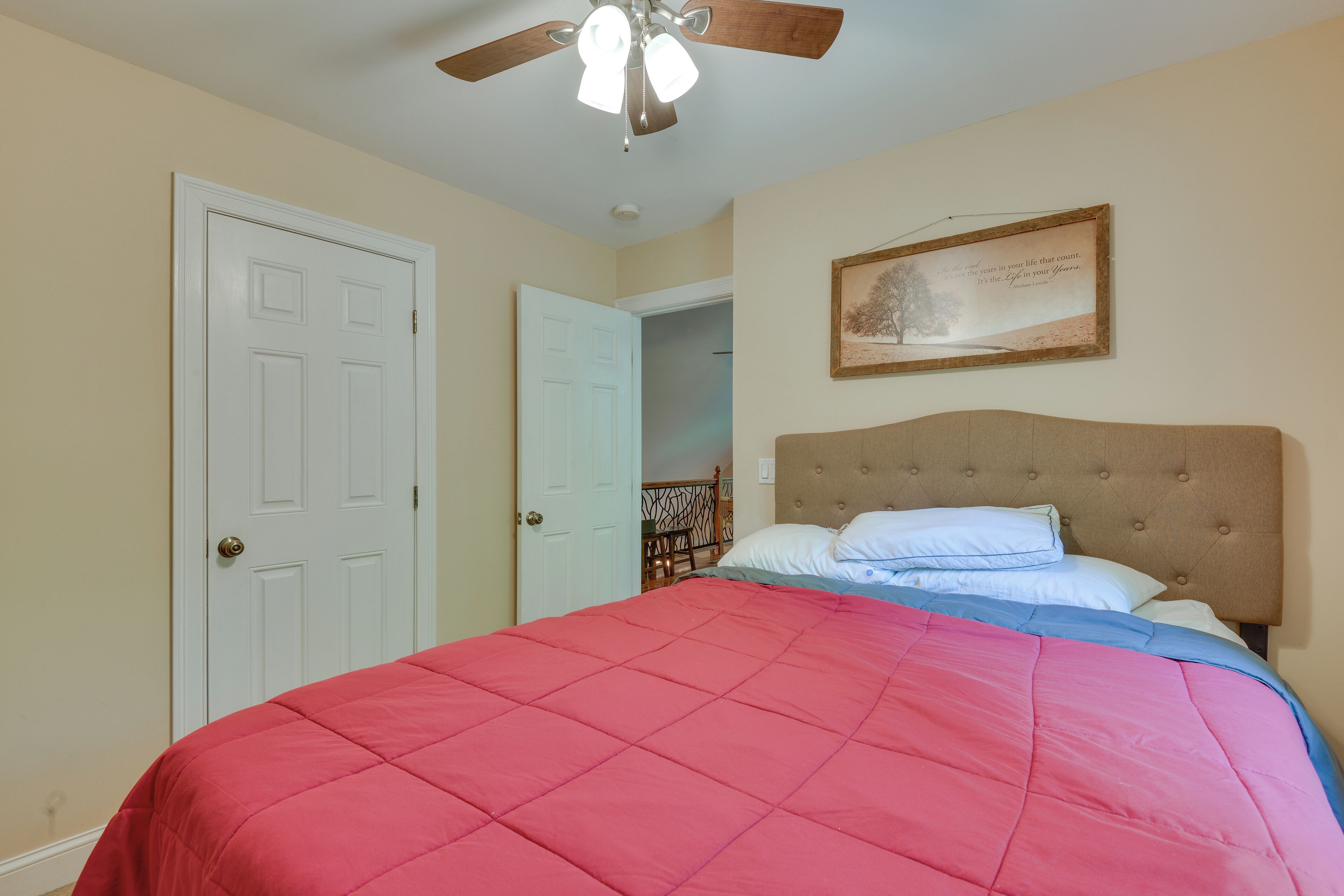 Une chambre à coucher avec un lit, un ventilateur de plafond, une porte et un tableau encadré au mur.