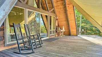 Relax on the deck with two comfortable chairs, adjacent to a large window offering a view of the surrounding trees.