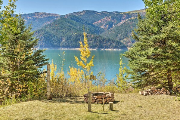 A lakeside view with a wooden bench, a pile of logs, and a flag. - Irwin A-frame Cabin w/ Deck & Mountain Views! (Irwin)
