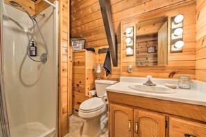 Une salle de bain rustique, aménagée dans une cabane en bois, comprenant une douche, des toilettes, un meuble-lavabo et un miroir avec éclairage.