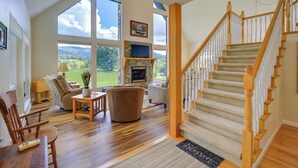 Un salón espacioso con una escalera de madera, ventanas amplias y una chimenea.