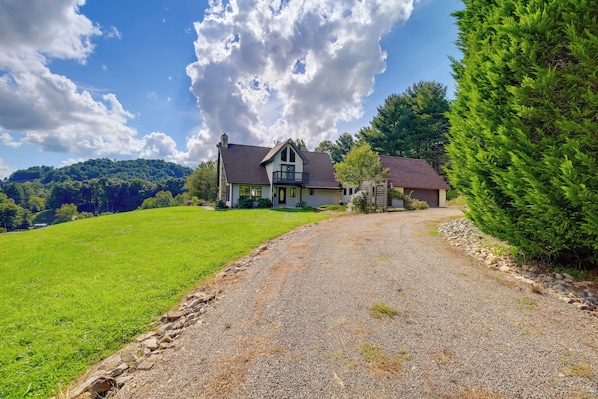 A two-story house with a gravel driveway leading to a wooden gate.