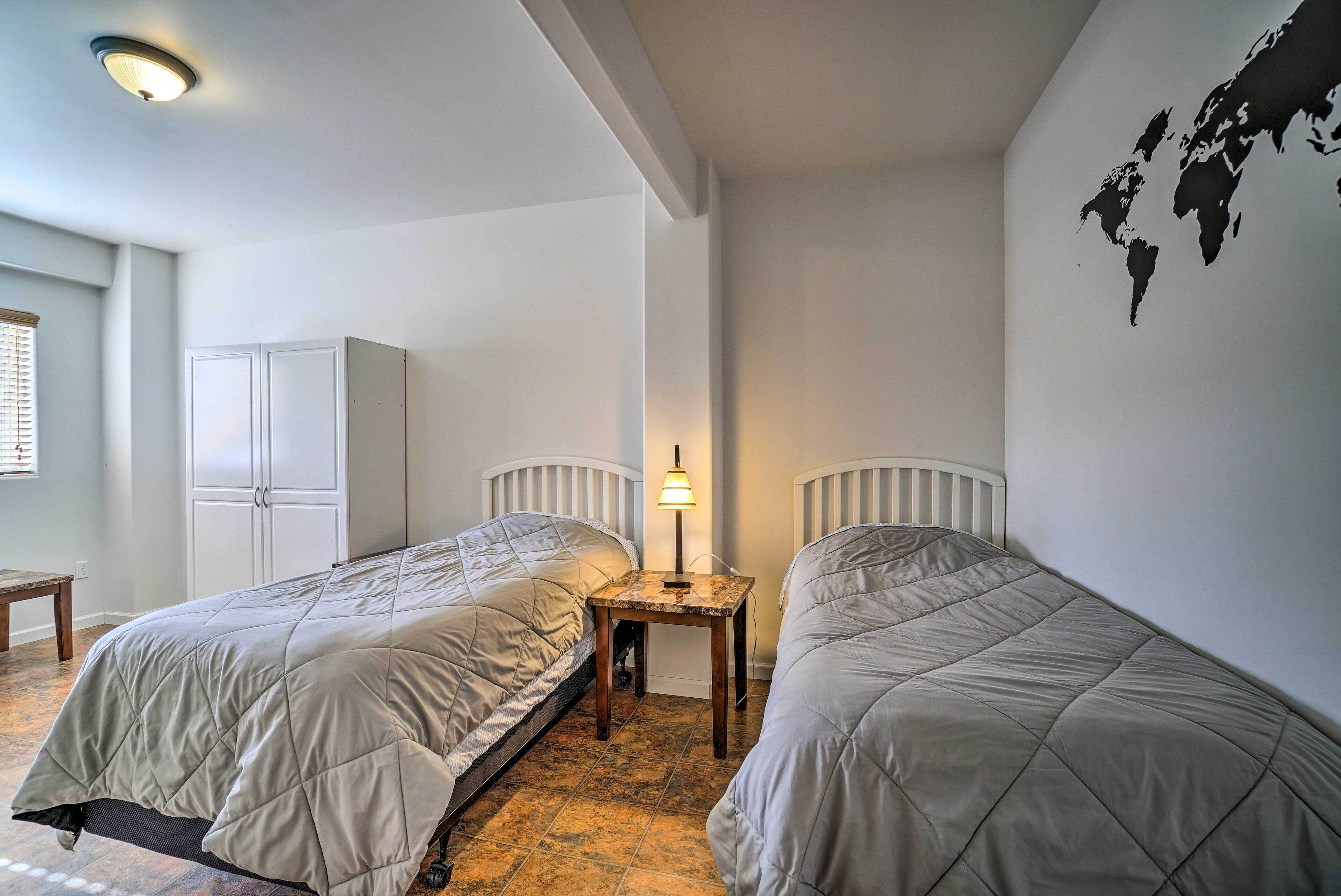Une chambre avec deux lits jumeaux, une table de chevet avec une lampe, une armoire et une carte du monde accrochée au mur.