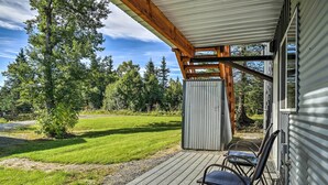Eine Holzterrasse mit Stühlen, ein Metallschuppen und ein Rasen mit Bäumen.