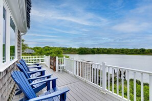 A wooden deck with blue Adirondack chairs, a white railing, and a view of a lake. - Cozy Narragansett Cottage w/ Dock & Outdoor Shower (Narragansett)