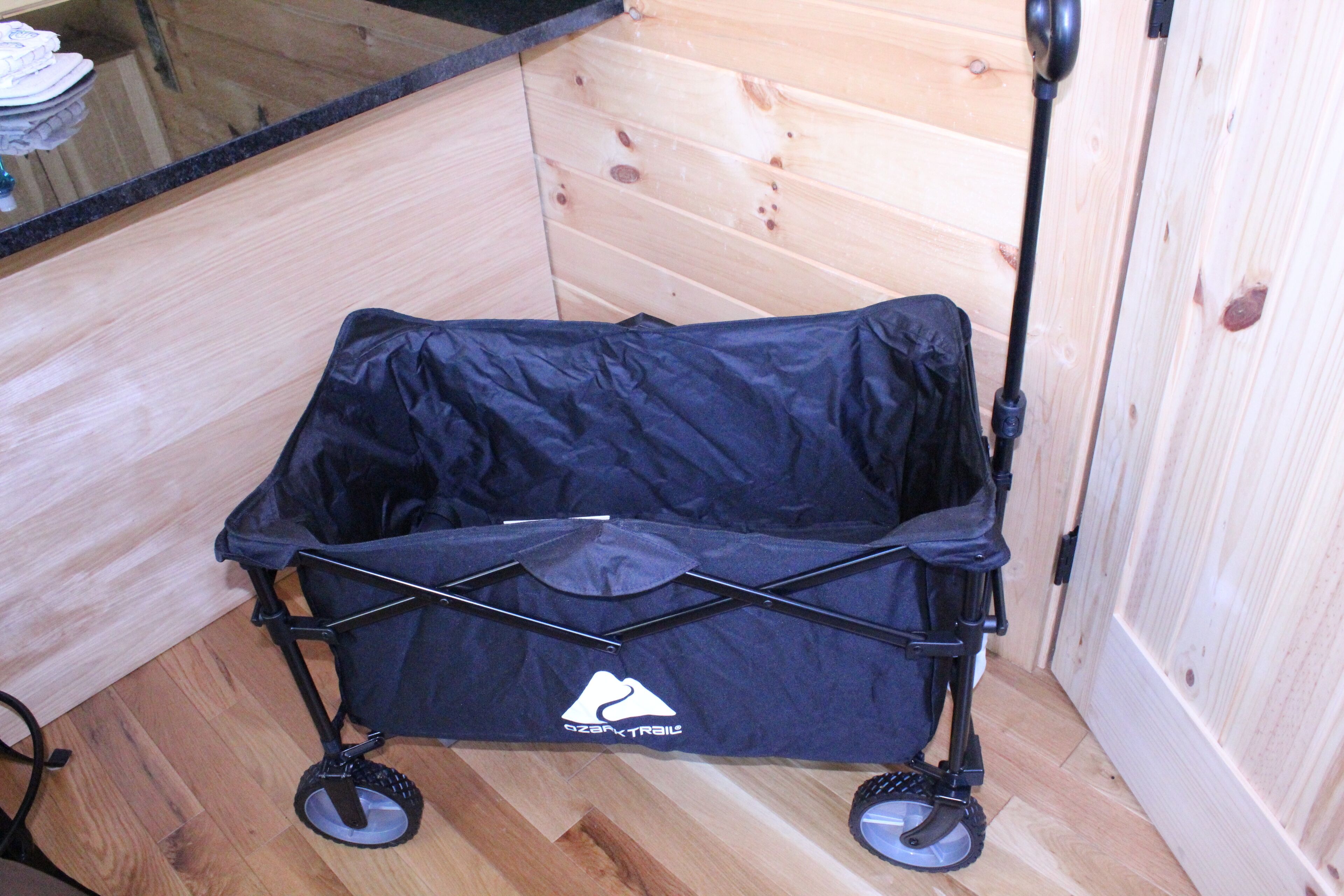 A black baby stroller with wheels and a canopy, placed on a wooden floor against a wooden wall.