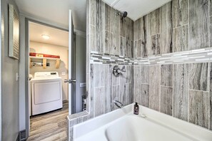 Ein modernes Badezimmer mit einer großen Badewanne, einer Dusche und einem Waschbereich, der durch eine offene Tür sichtbar ist.