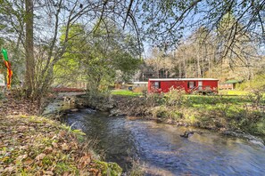A red building with a small bridge over a stream, surrounded by trees and greenery. - Bring a Pet: Smoky Mtn Vacation Rental w/ Yard! (Whittier)
