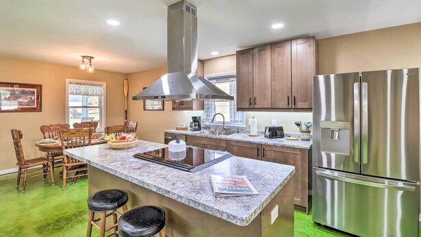 A modern kitchen with a central island, stainless steel appliances, wooden cabinets, and a dining area with chairs and a table. - Brand New Cotter Home, Walk to Trout Fishing! (Cotter)