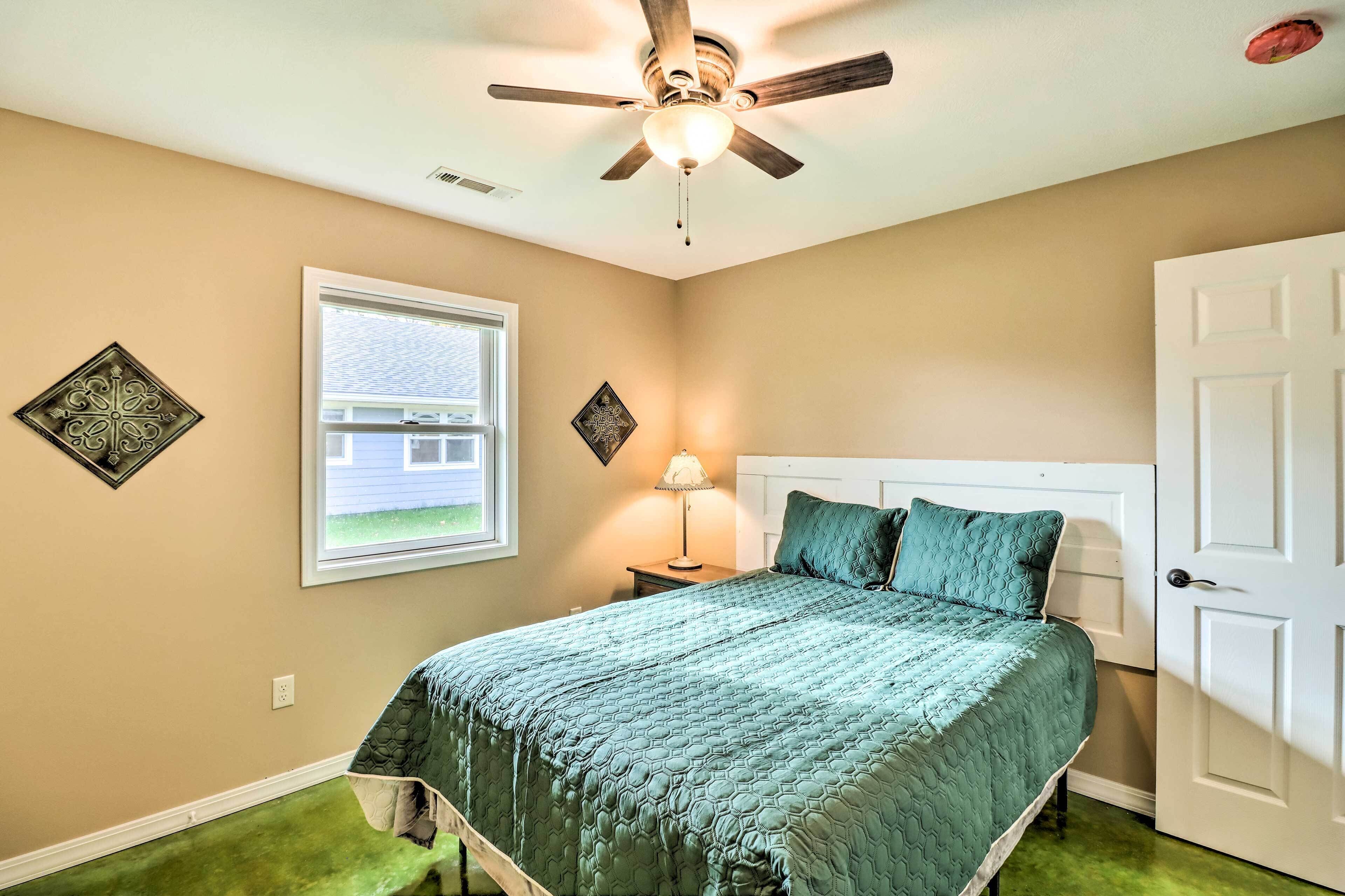 Une chambre à coucher comprenant un lit, un ventilateur de plafond, une fenêtre et deux éléments de décoration murale.