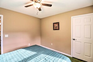 Une chambre à coucher avec un lit, un ventilateur de plafond, une porte blanche et un tableau encadré au mur.