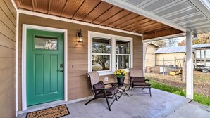 A house with a green door, two windows, a porch with two chairs and a table, and a welcome mat. - Brand New Cotter Home, Walk to Trout Fishing! (Cotter)