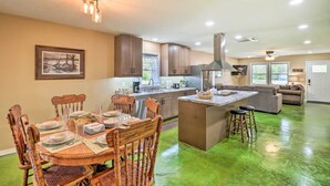 A modern kitchen with a central island, wooden chairs, and a dining table set for four. - Brand New Cotter Home, Walk to Trout Fishing! (Cotter)