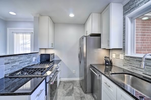 Een moderne keuken met roestvrijstalen apparatuur, witte kastjes en een zwart aanrecht.