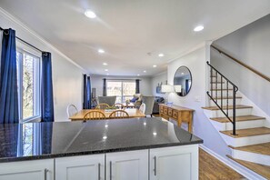 Eine Küche mit einer Granit Arbeitsplatte, weißen Schränken, einem Essbereich mit Holztisch und Stühlen sowie einer Treppe mit Holzstufen und einem schwarzen Geländer.