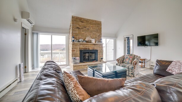 A spacious living room with a stone fireplace, leather sofas, a glass coffee table, and a flat-screen TV mounted on the wall. - Alpine Lake Resort Home: Stunning Lake Views! (Terra Alta)