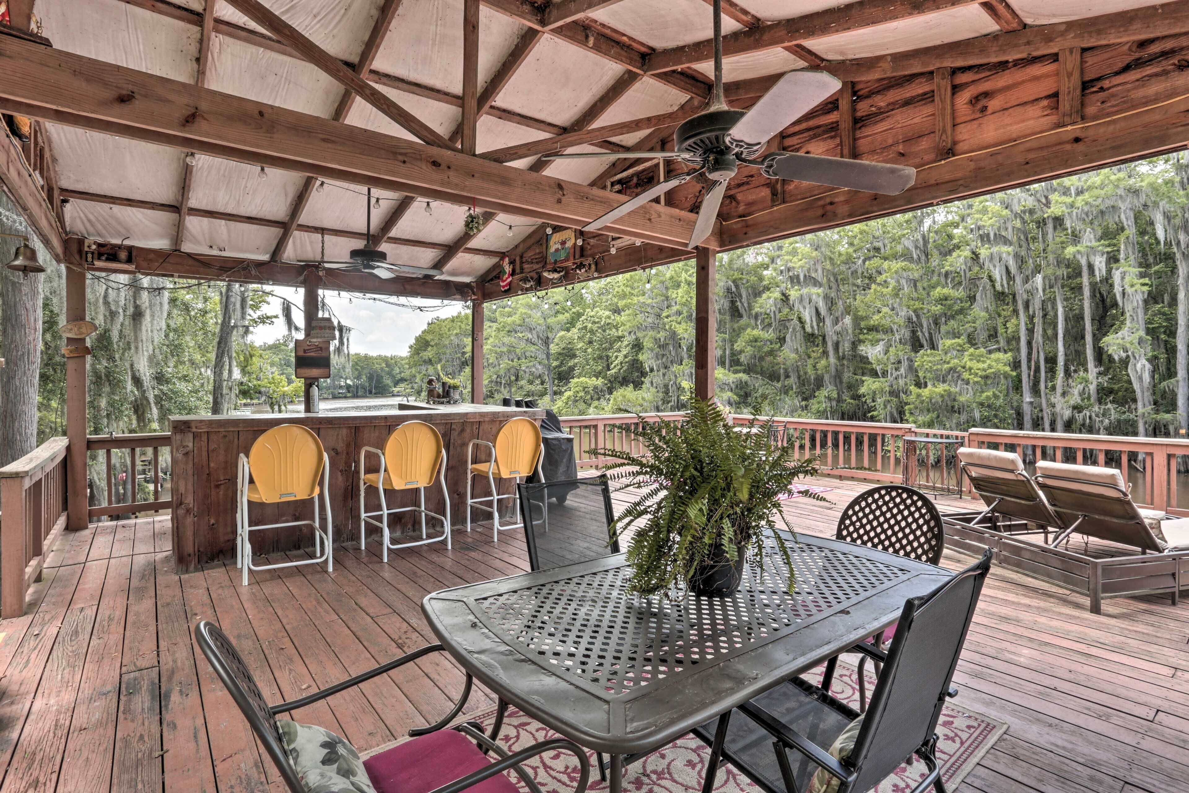 A covered outdoor deck with a table and chairs, a bar area, and a view of the surrounding forest.