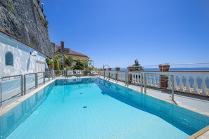 Une piscine à l’eau d’un bleu cristallin, entourée d’une balustrade blanche, et offrant une vue sur une falaise et un bâtiment.