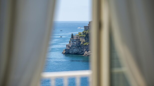 Vista costera a través de una ventana, con un edificio en un acantilado sobre el mar.