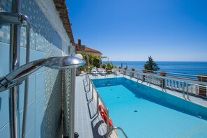 Un espace piscine offrant une vue dégagée sur l’océan, une bouée de sauvetage et une rambarde en métal.