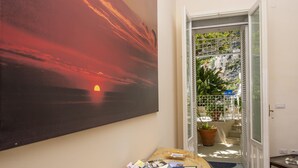 Habitación con un cuadro grande de un atardecer, vistas despejadas del exterior a través de un ventanal y una mesa con revistas.
