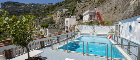 Una piscina sul tetto con vista su una collina, sedie a sdraio bianche e una pianta in vaso.