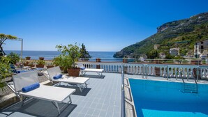 Una piscina en la azotea con sillones de descanso y plantas en macetas, con vistas a la costa.
