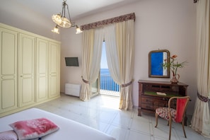 A bedroom with a bed, a chair, a dresser, a mirror, and a view of the sea through large curtains. - Villa Arte- Luxurious Villa in Ravello (Minori)