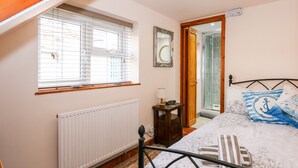 Un dormitorio con cama, una mesita de noche con lámpara, una ventana con persianas, un radiador y una puerta que da a un baño.