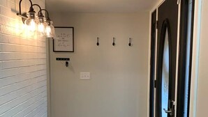 Un pasillo con pared de ladrillo blanco, puerta negra y lámpara con bombillas expuestas.
