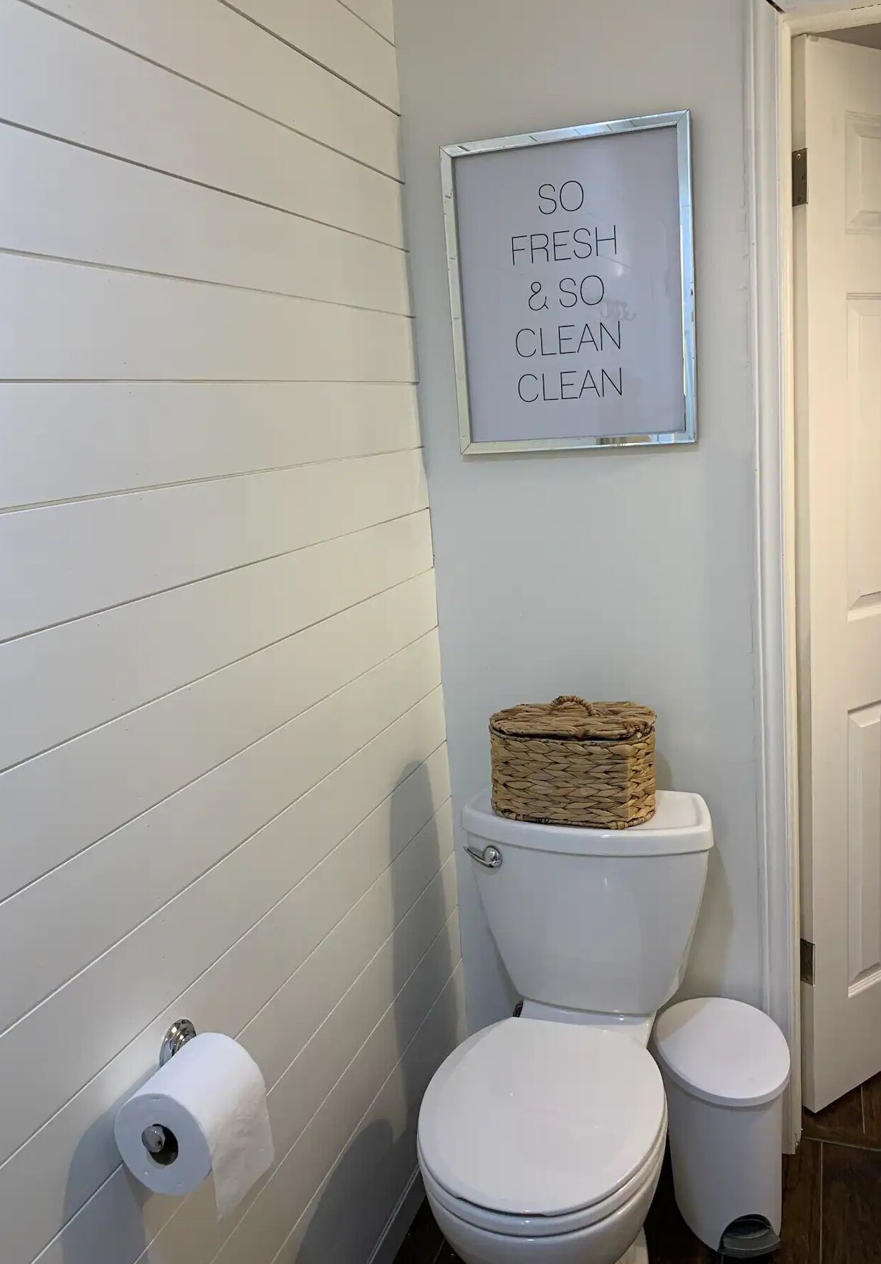 A bathroom with a toilet, a trash bin, and a framed sign on the wall.
