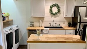 Una cocina moderna con armarios blancos, encimera de madera, lavadero empotrado y refrigerador de acero inoxidable.