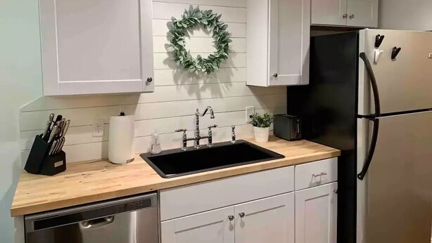 Una cocina con armarios blancos, un lavamanos negro, electrodomésticos de acero inoxidable y un adorno floral en la pared.