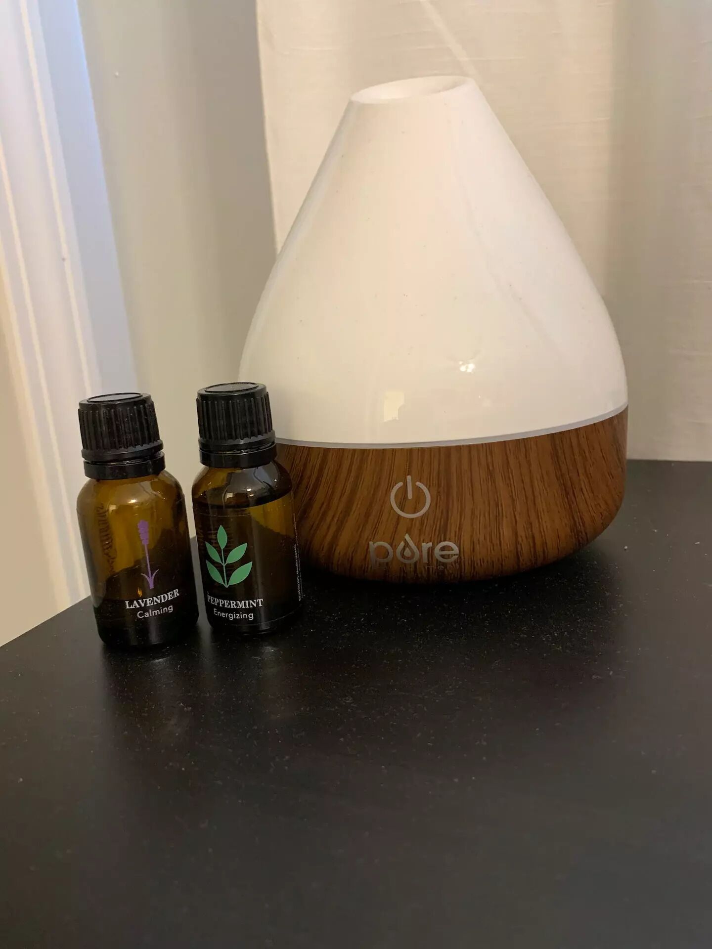 A diffuser with two essential oil bottles labeled 'Lavender Calming' and 'Peppermint Energizing' on a dark surface.