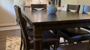 Un comedor con una mesa y sillas de madera oscura, un jarrón decorativo y una cocina al fondo.