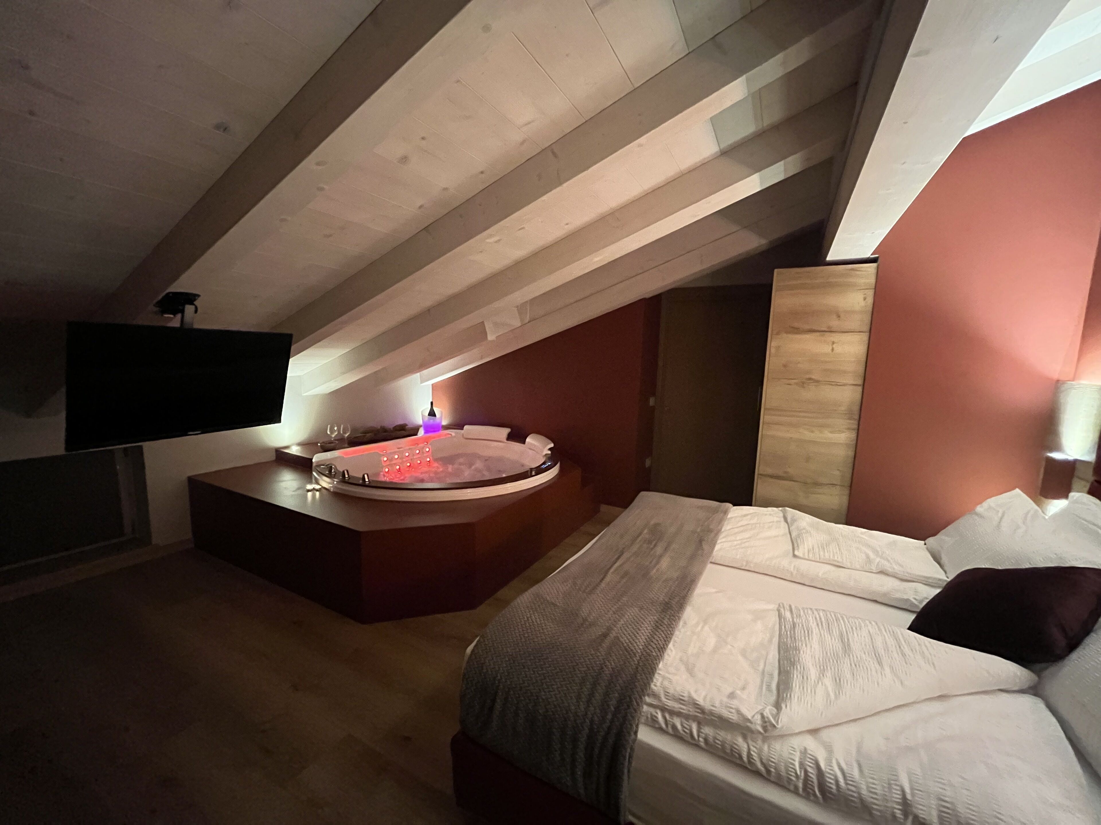 Une chambre dotée d’un grand lit, d’un petit coin salon avec un jacuzzi et d’un téléviseur fixé au mur.