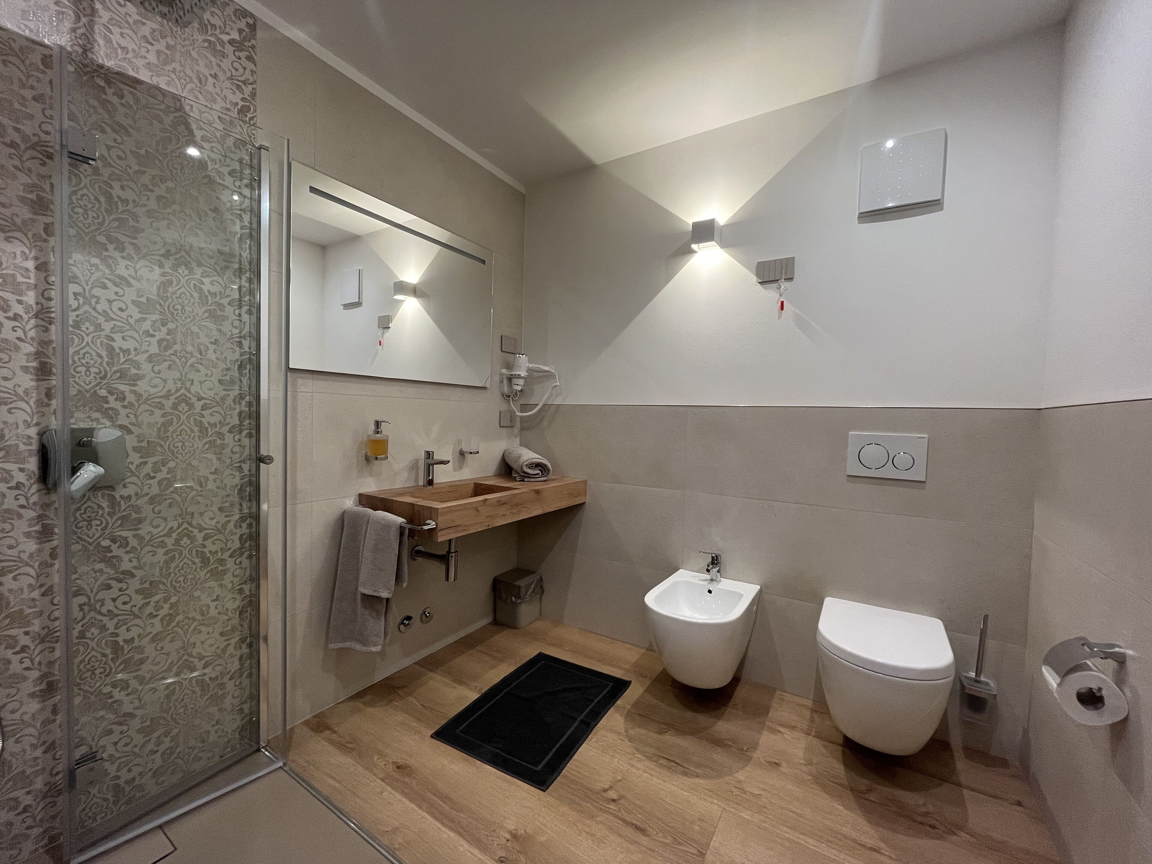 Un bagno moderno con cabina doccia in vetro, mobile lavabo in legno, un bidet e un water.