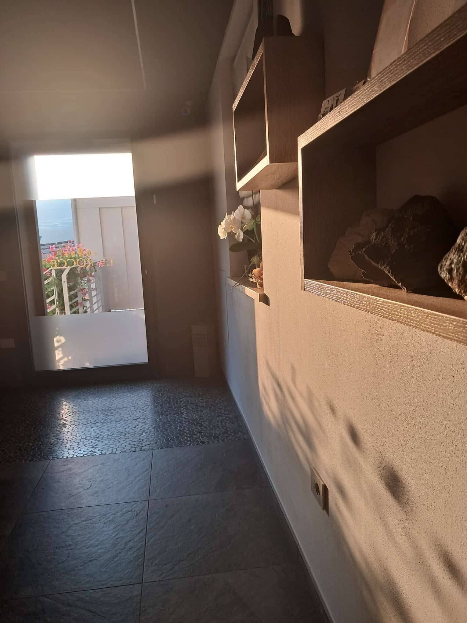 Een gang met uitzicht op een balkon, een klein schap met decoratieve objecten en een structuurwand.