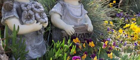 Two garden statues of children holding flowers, surrounded by a variety of plants and flowers.