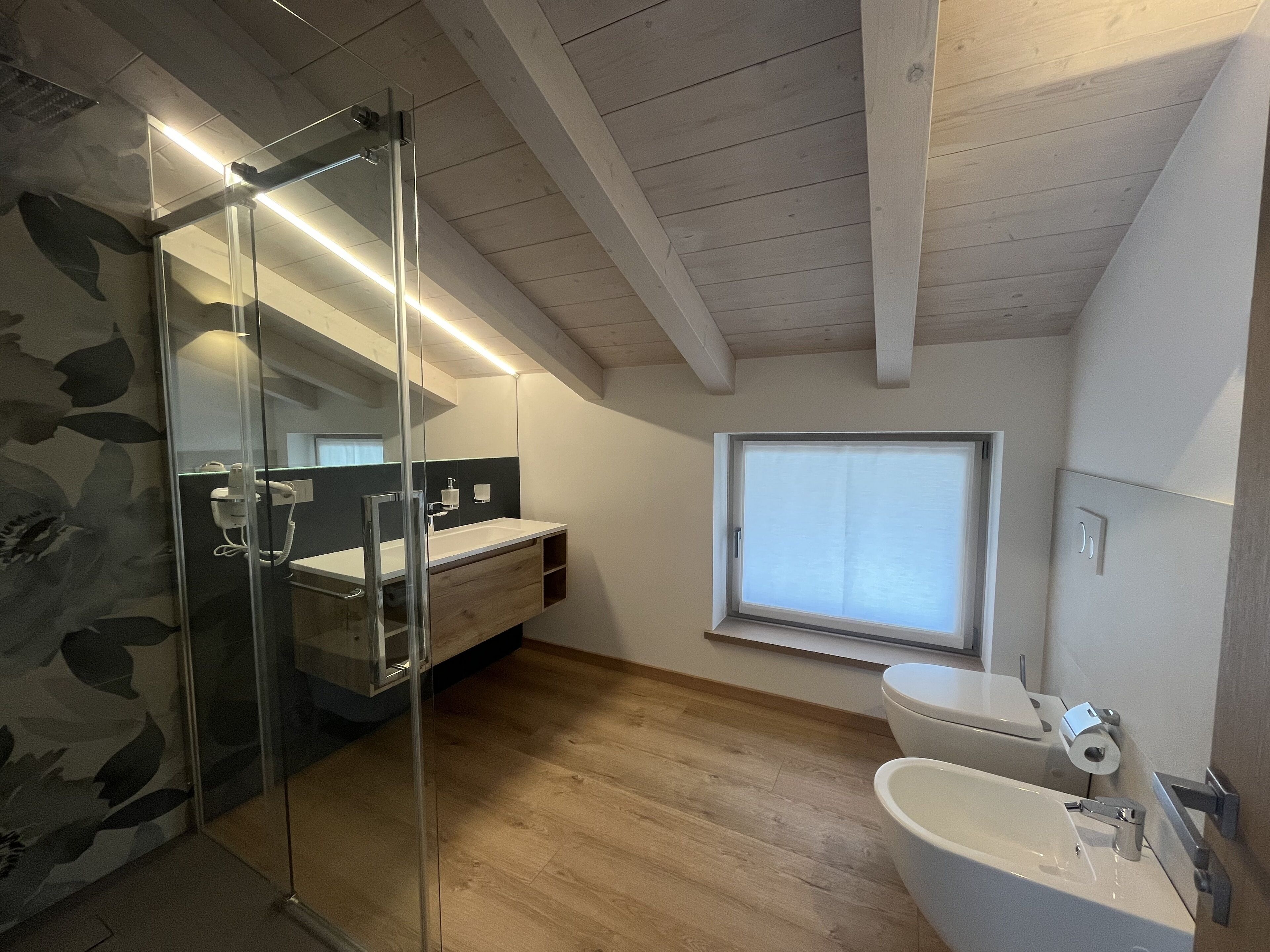 Ein modernes Badezimmer mit Duschkabine aus Glas, einem Holzwaschtisch, einer Toilette und einem Fenster für natürliches Licht.