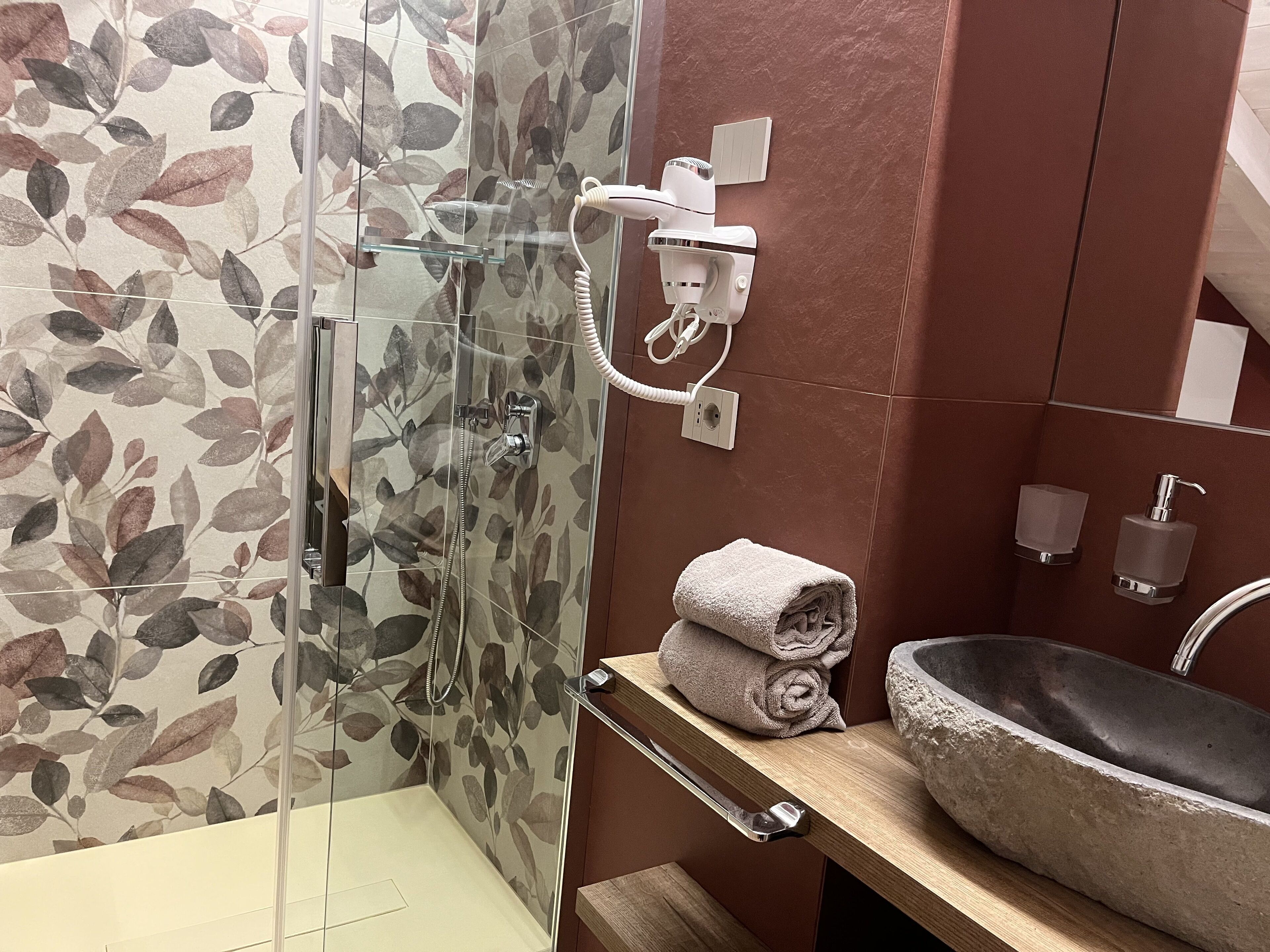 Un baño con cabina de ducha de vidrio, tocador de madera con lavabo de piedra y perchero para toallas.